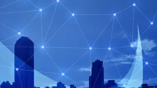 ビル群のシルエットの上に、光の点を結ぶネットワーク線が広がる青い画像